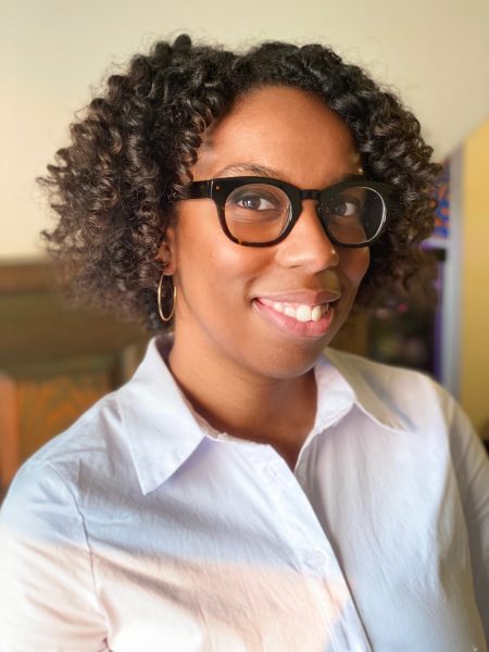 A headshot of Jessica Womack. She is a Black woman with curly hair and glasses wearing a white shirt.