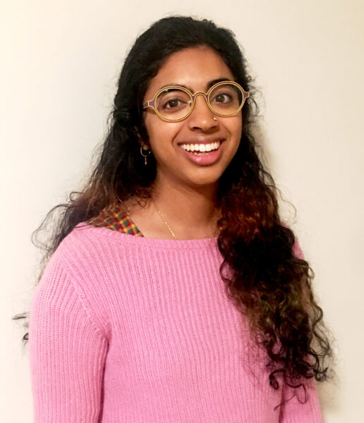 A photograph of Bhavani Srinivas, a young, Indian-American woman with curly hair. She is smiling widely and she wears glasses.