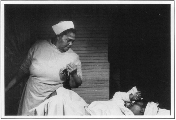 A black and white still showing midwife Mary Francis Coley attending to a patient.