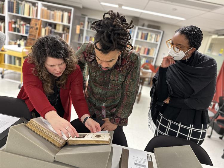 Photograph of three people, Holly Hatheway, Nate Lewis, and Jessica Womack, in Princeton's Special Collections examining a book.